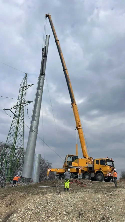 Automacara ridicând lângă piloni electrici, pe un teren viran.