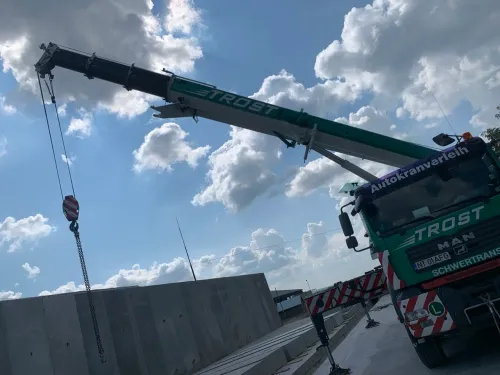 Automacara ridicând un panou de beton prefabricat, pe un șantier deschis.