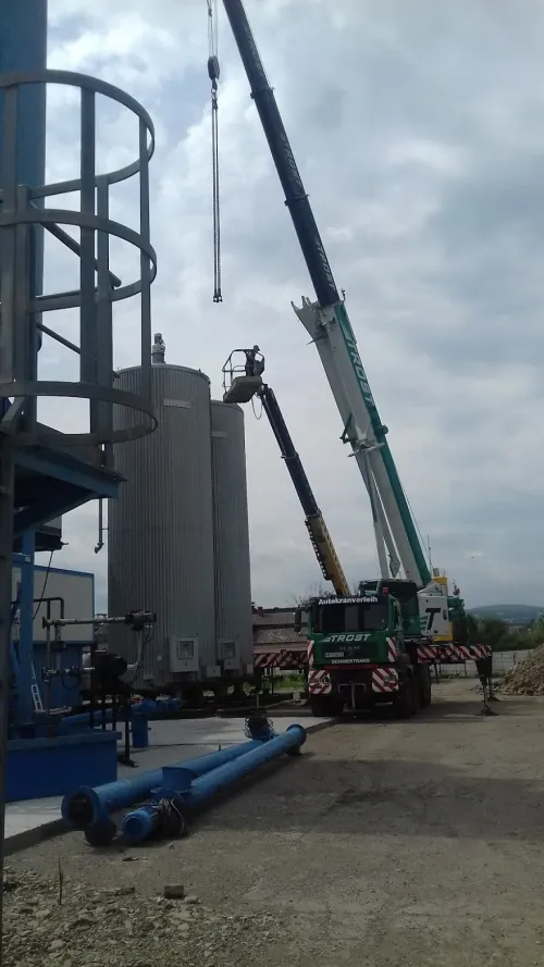 Două automacarale manevrând un rezervor cilindric metalic, la un șantier industrial.