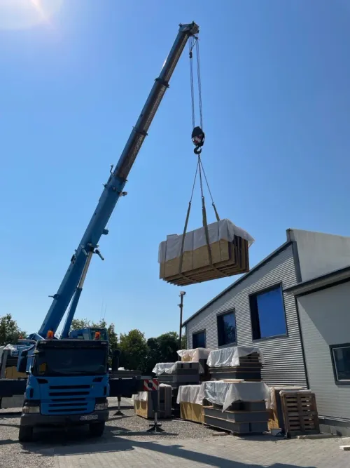 Automacara ridicând un panou izolator învelit, lângă o clădire industrială.