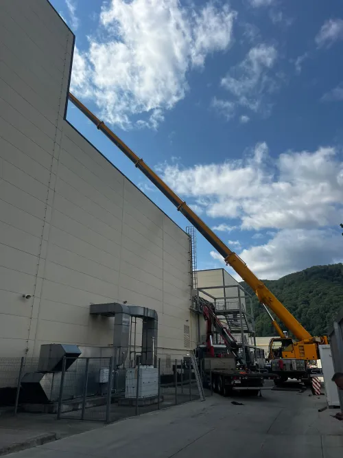 Automacara cu brațul extins de-a lungul acoperișului unei hale industriale.