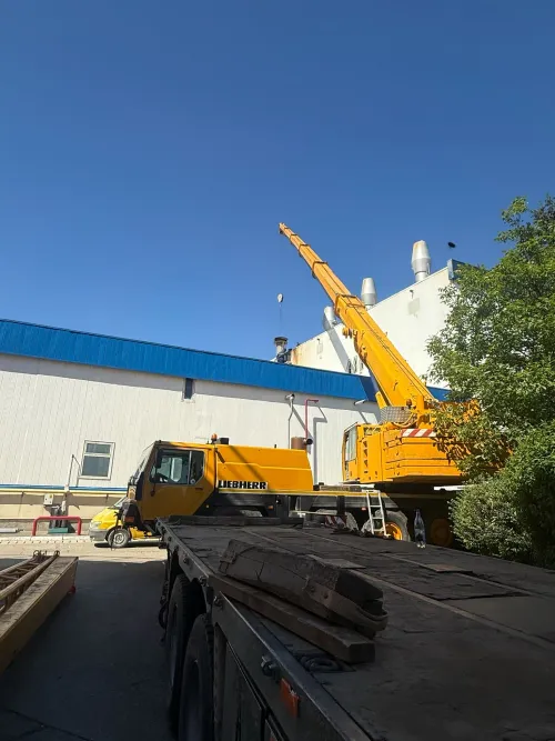 Automacara cu brațul extins spre acoperișul unei clădiri industriale.